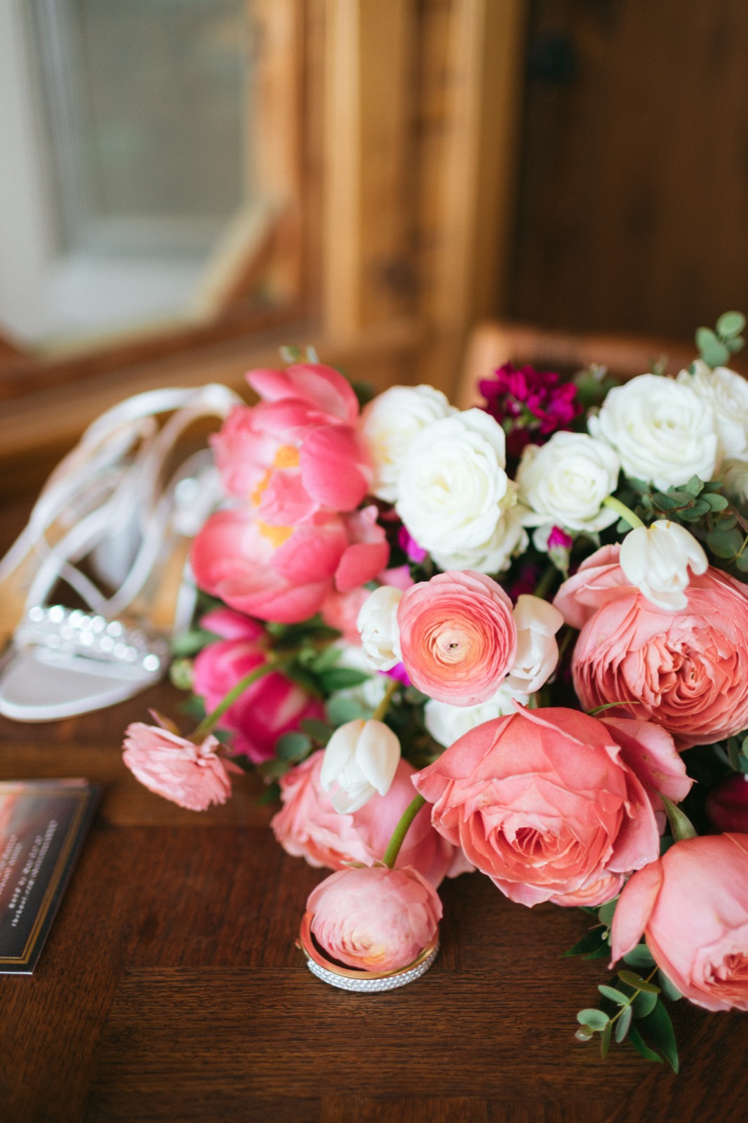 Coral peonies, ivory garden roses, and ranunculus in Melissa's bridal bouquet beside her heels and wedding band on warm wood at Madden's on Gull Lake — Tim Larsen Photography, Brainerd Lakes MN