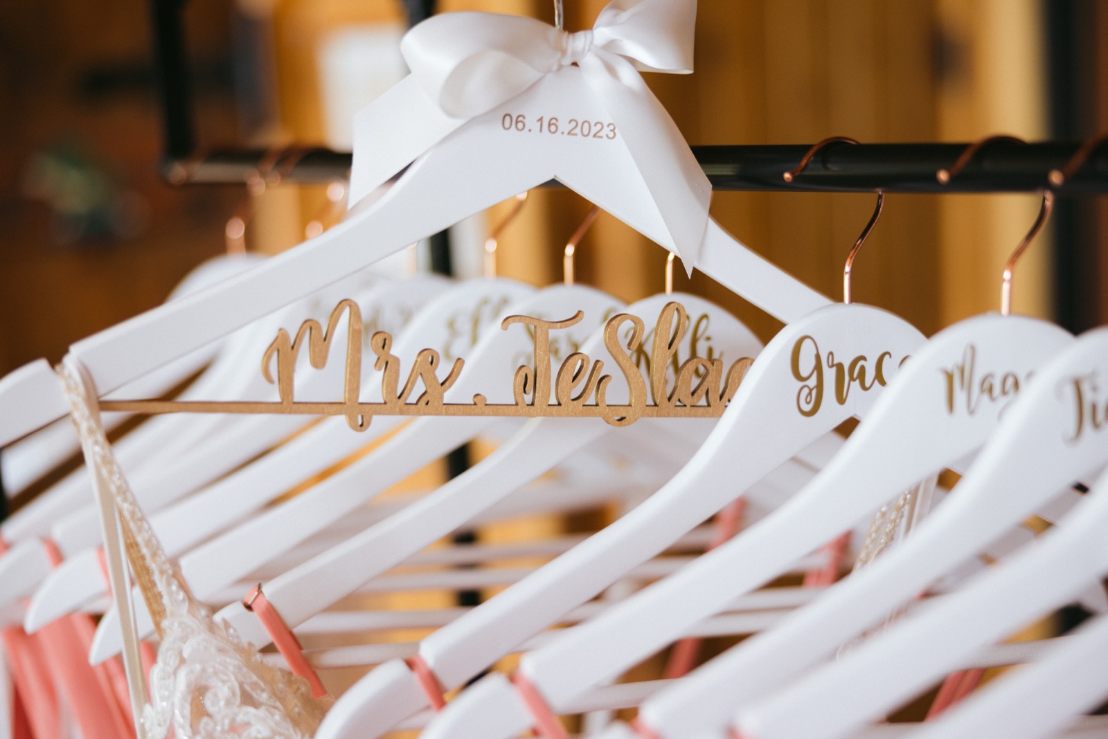 Custom white wooden hangers with gold cursive script — the Mrs. hanger reads 06.16.2023 in gold, surrounded by matching bridesmaid hangers in the bridal suite — Tim Larsen Photography, Brainerd Lakes MN