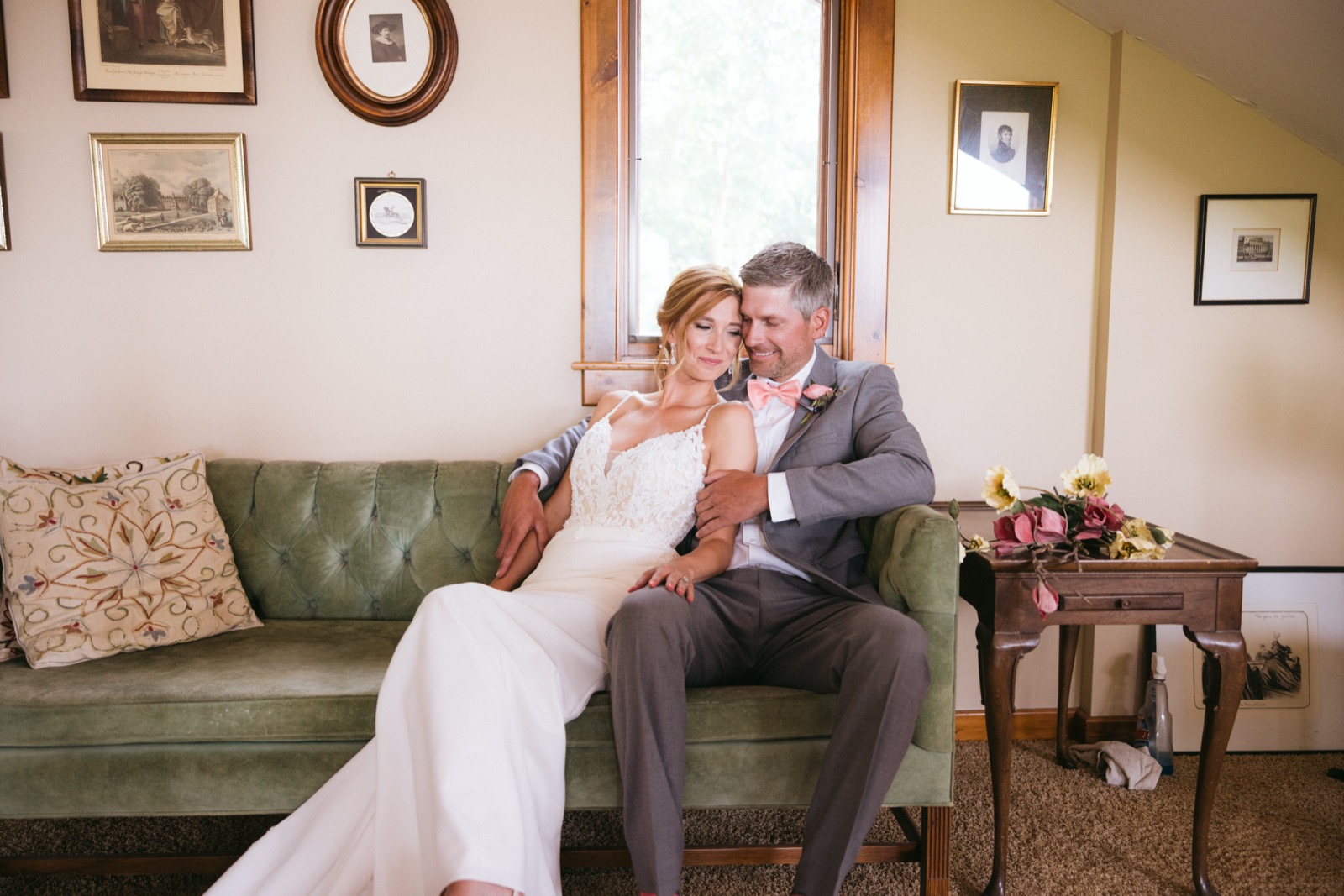 Melissa and Kody seated together on a green velvet sofa in a Madden's sitting room, framed by a window and gallery wall artwork — Tim Larsen Photography, Brainerd Lakes MN
