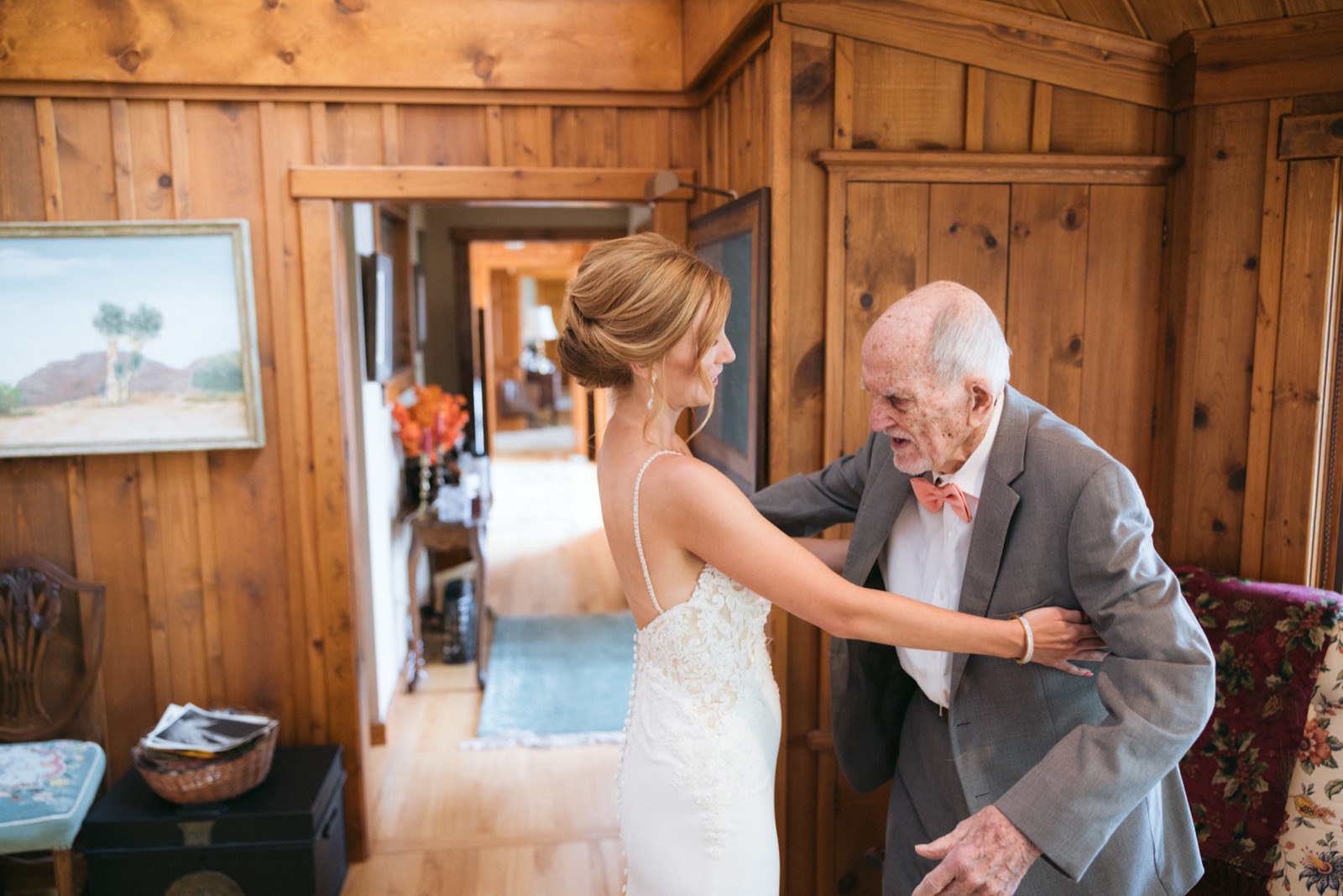 Melissa reaches out to embrace her father in a gray suit and coral bow tie inside a warm wood-paneled cabin room at Madden's — Tim Larsen Photography, Brainerd Lakes MN