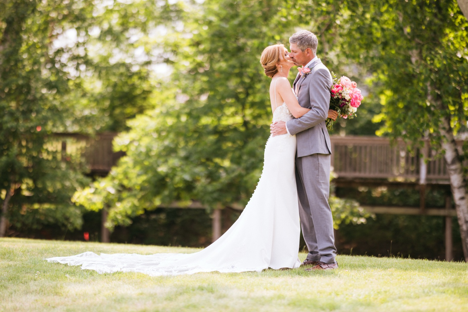 Melissa and Kody anchored on the resort lawn at Madden's, her train sweeping across the grass with birch trees and the lodge balconies framing them — Tim Larsen Photography, Brainerd Lakes MN