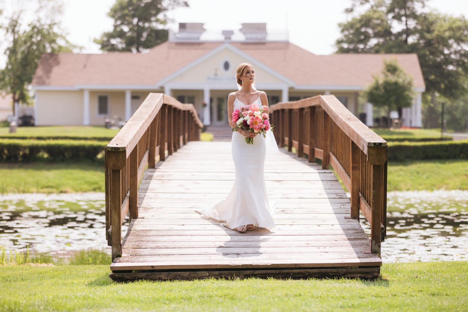 Melissa centered on a wooden footbridge over a lily pond at Madden's, the lodge facade rising symmetrically behind her — Tim Larsen Photography, Brainerd Lakes MN
