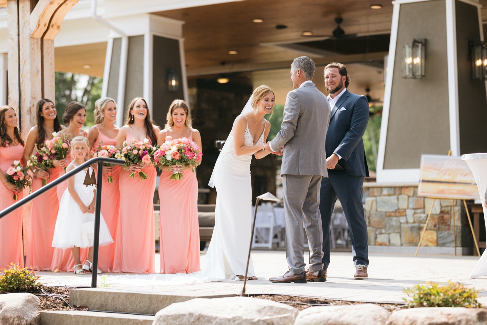 Melissa laughing mid-vow as Kody holds her hands during the ceremony at Madden's pavilion, coral-clad bridesmaids reacting on the left — Tim Larsen Photography, Brainerd Lakes MN