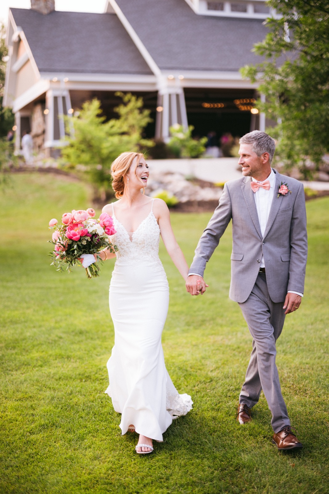 Melissa and Kody walk hand in hand on the lawn outside the Madden's lodge, string lights and lodge architecture warm behind them — Tim Larsen Photography, Brainerd Lakes MN