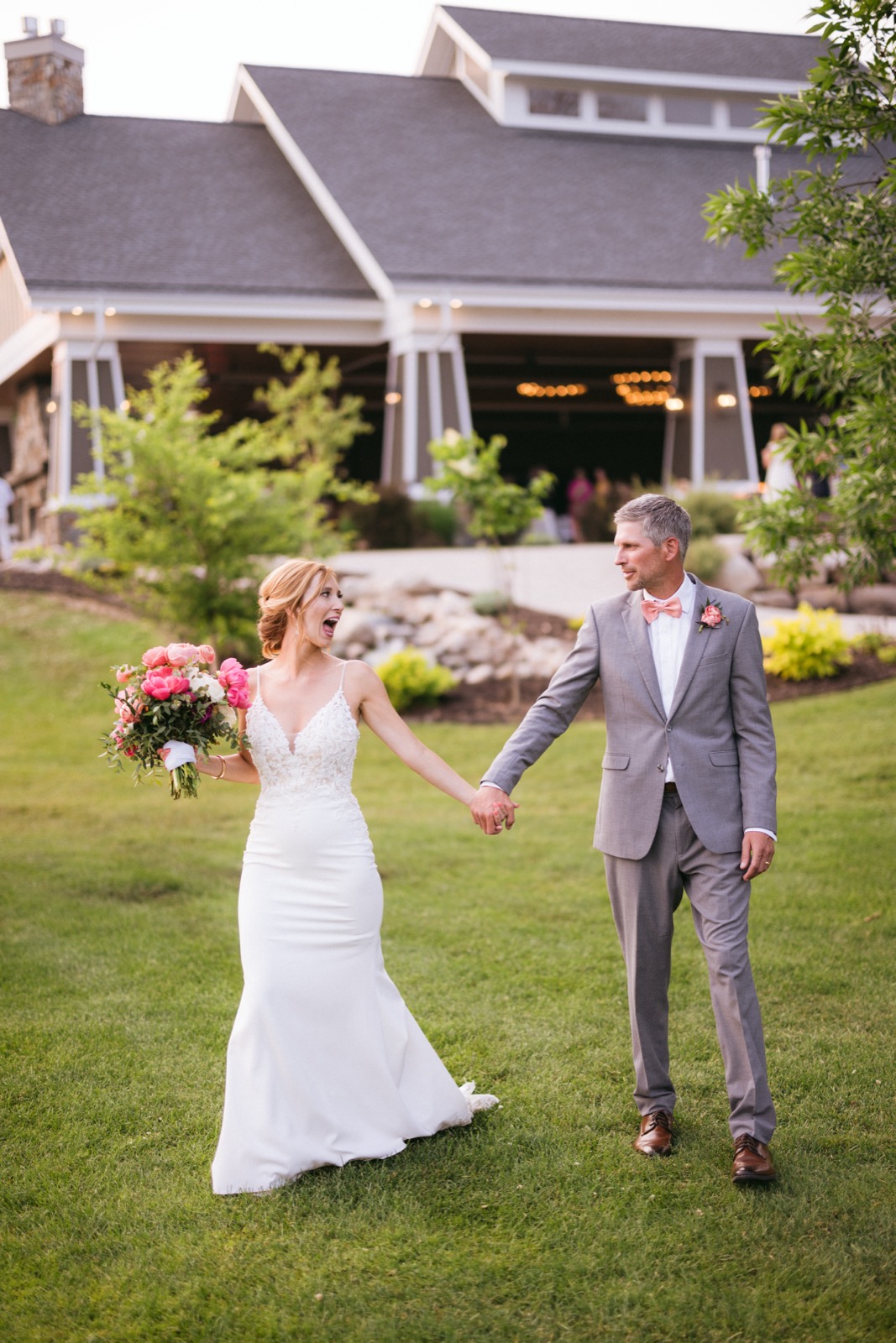 Melissa and Kody hold hands walking across the lawn at Madden's, the open-air pavilion looming behind, Melissa mid-laugh — Tim Larsen Photography, Brainerd Lakes MN