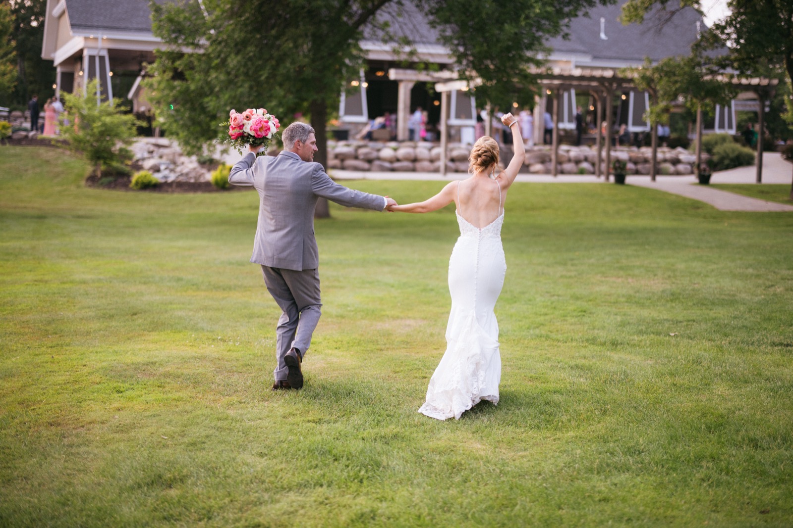 Melissa and Kody walking away from camera toward the lodge at Madden's, her arm raised in triumph across the lawn — Tim Larsen Photography, Brainerd Lakes MN