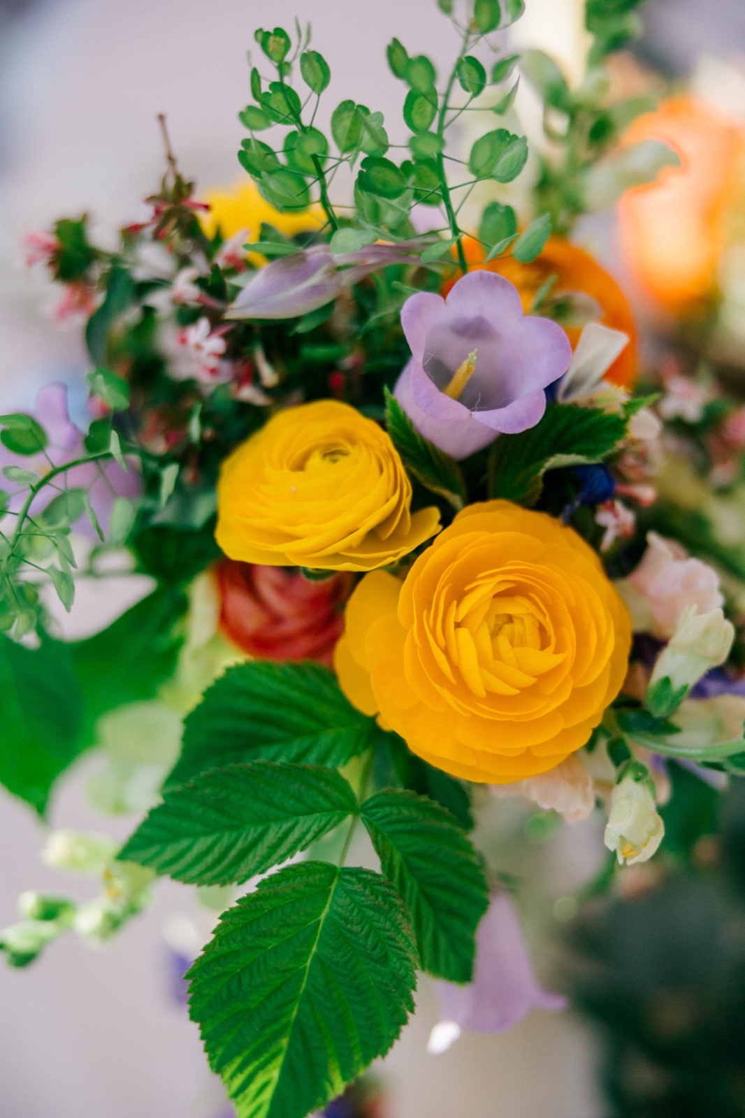 Close-up of a bridal bouquet featuring yellow ranunculus, lavender bellflowers, peach roses, and trailing greenery — Tim Larsen Photography, Brainerd Lakes MN