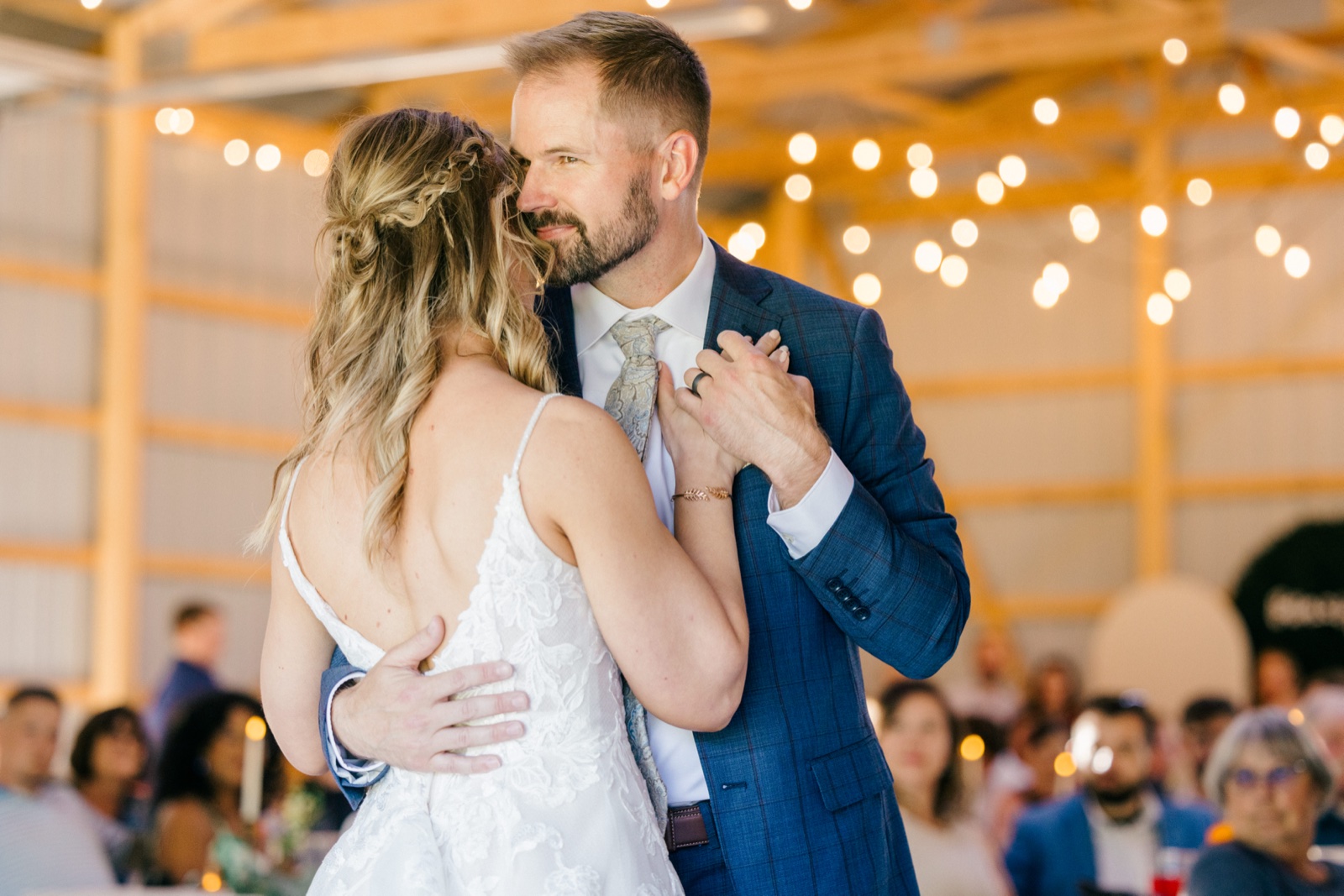 The groom holds the bride close during their first dance under string lights in an open-sided pavilion as guests watch from the edges — Tim Larsen Photography, Brainerd Lakes MN