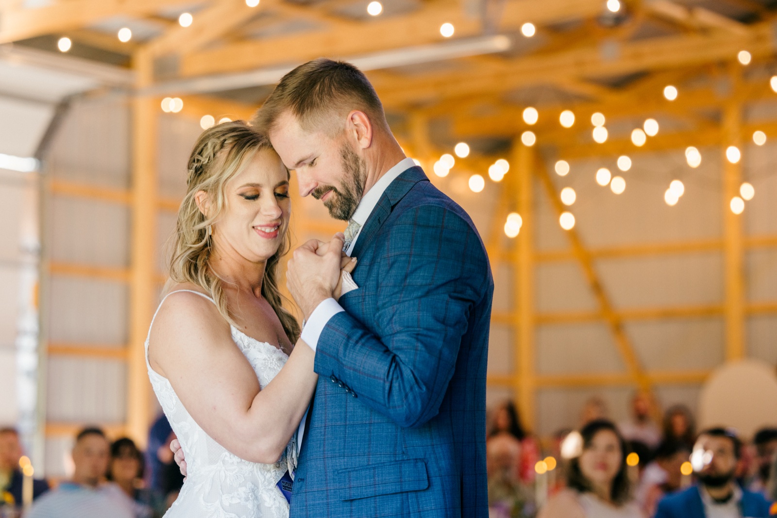 The bride smiles with closed eyes as the groom presses his forehead to hers during their first dance, with string lights and an open-air wooden pavilion behind them — Tim Larsen Photography, Brainerd Lakes MN