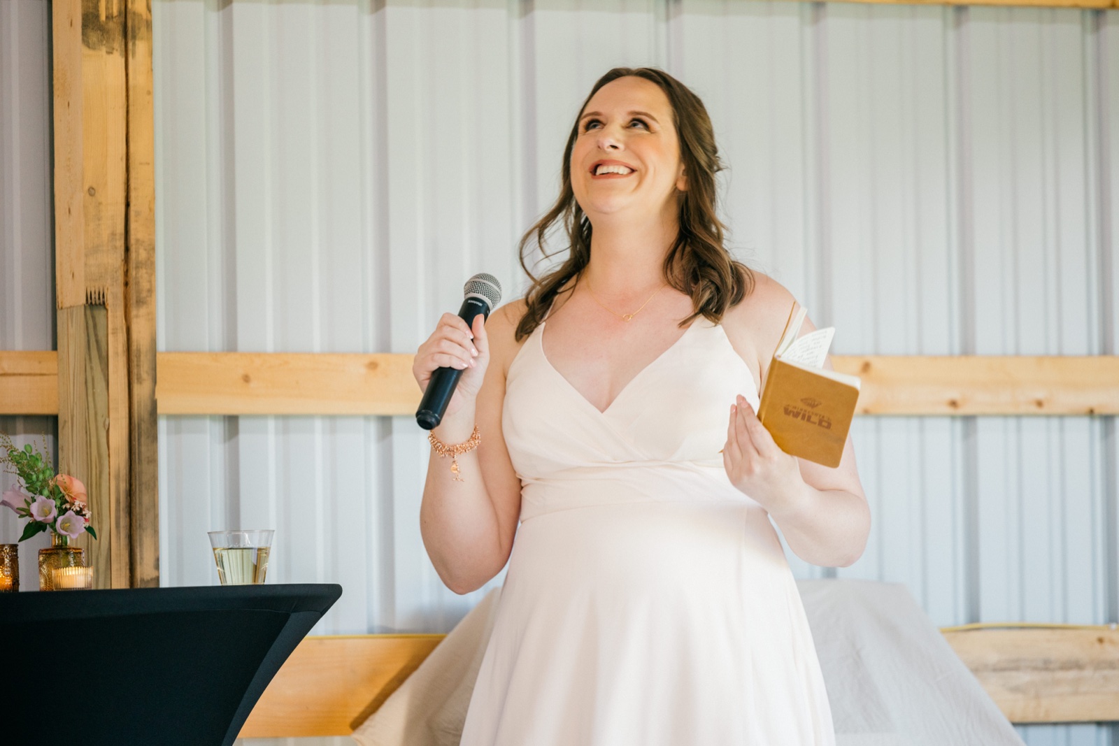 The bride laughs and looks upward while holding a microphone in one hand and a small notebook of speech notes in the other — Tim Larsen Photography, Brainerd Lakes MN