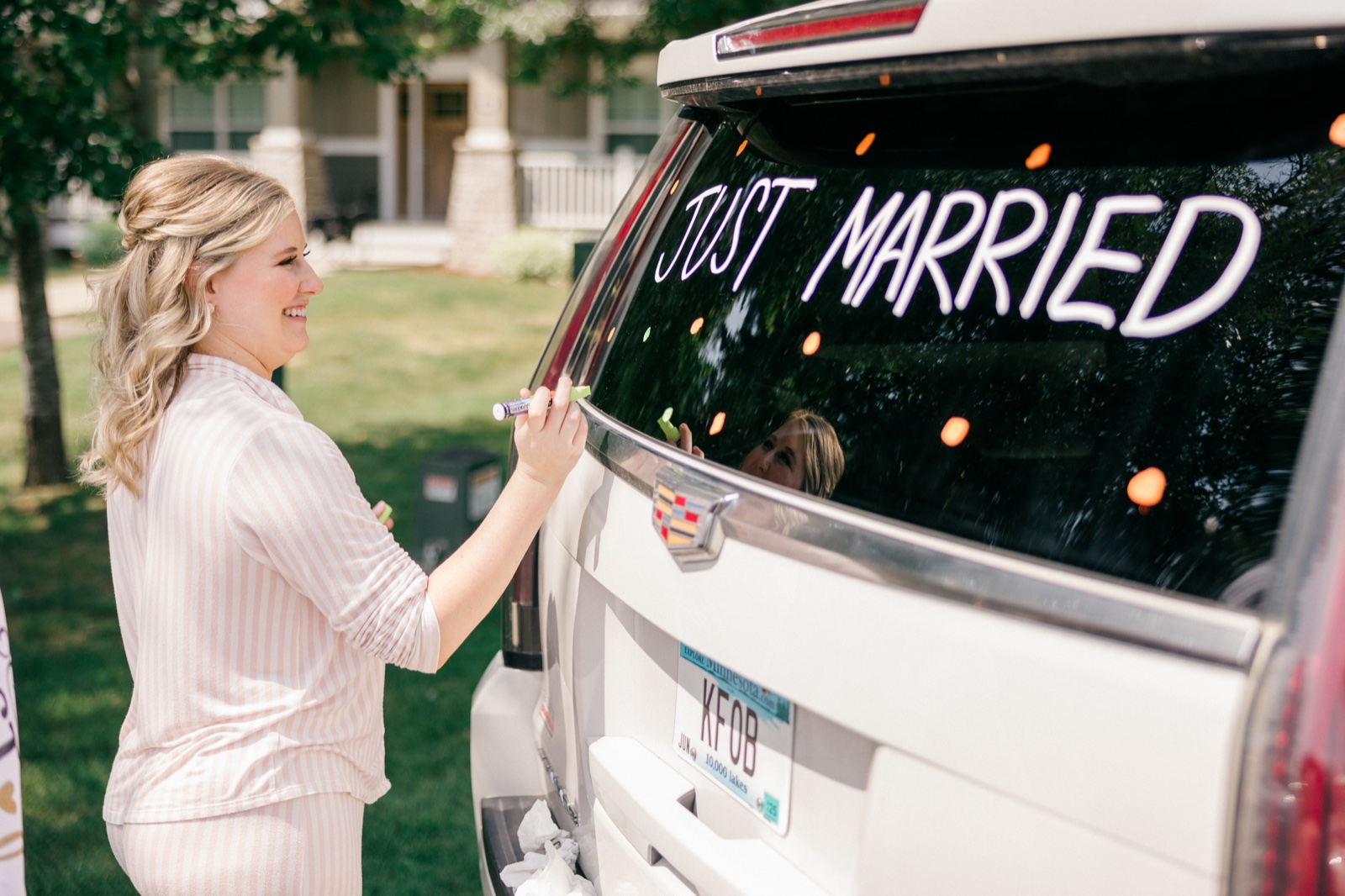 The bride in striped pajamas writes Just Married on the rear window of a white SUV outside the resort — Tim Larsen Photography, Brainerd Lakes MN