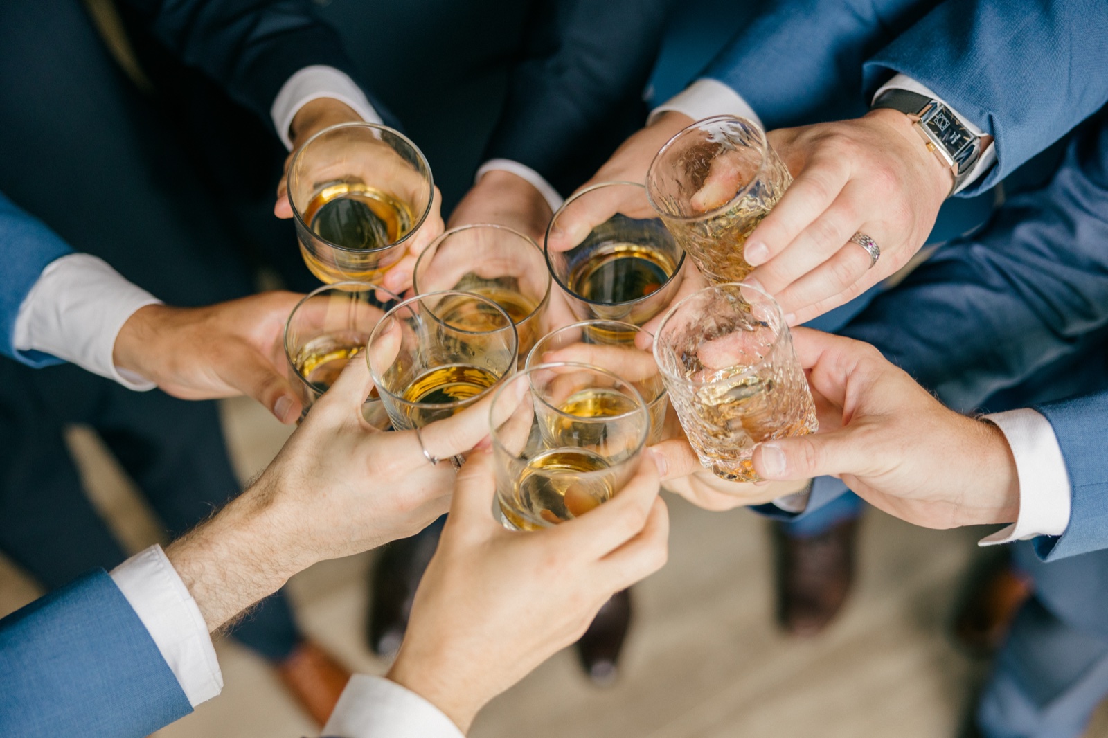 Overhead view of Mats and his groomsmen clinking whiskey glasses together in a circle, suited arms radiating outward — Tim Larsen Photography, Brainerd Lakes MN