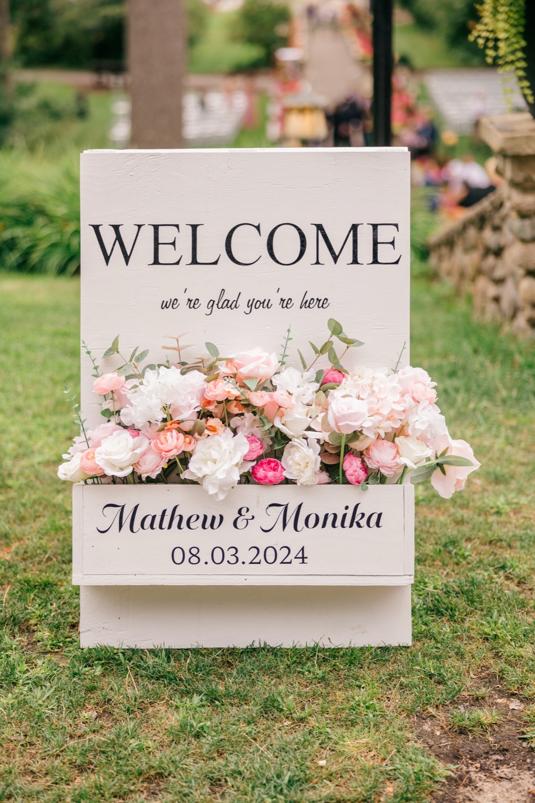 White wooden welcome sign with pink florals on the lawn outside the Grand View Lodge ceremony — Tim Larsen Photography, Brainerd Lakes MN