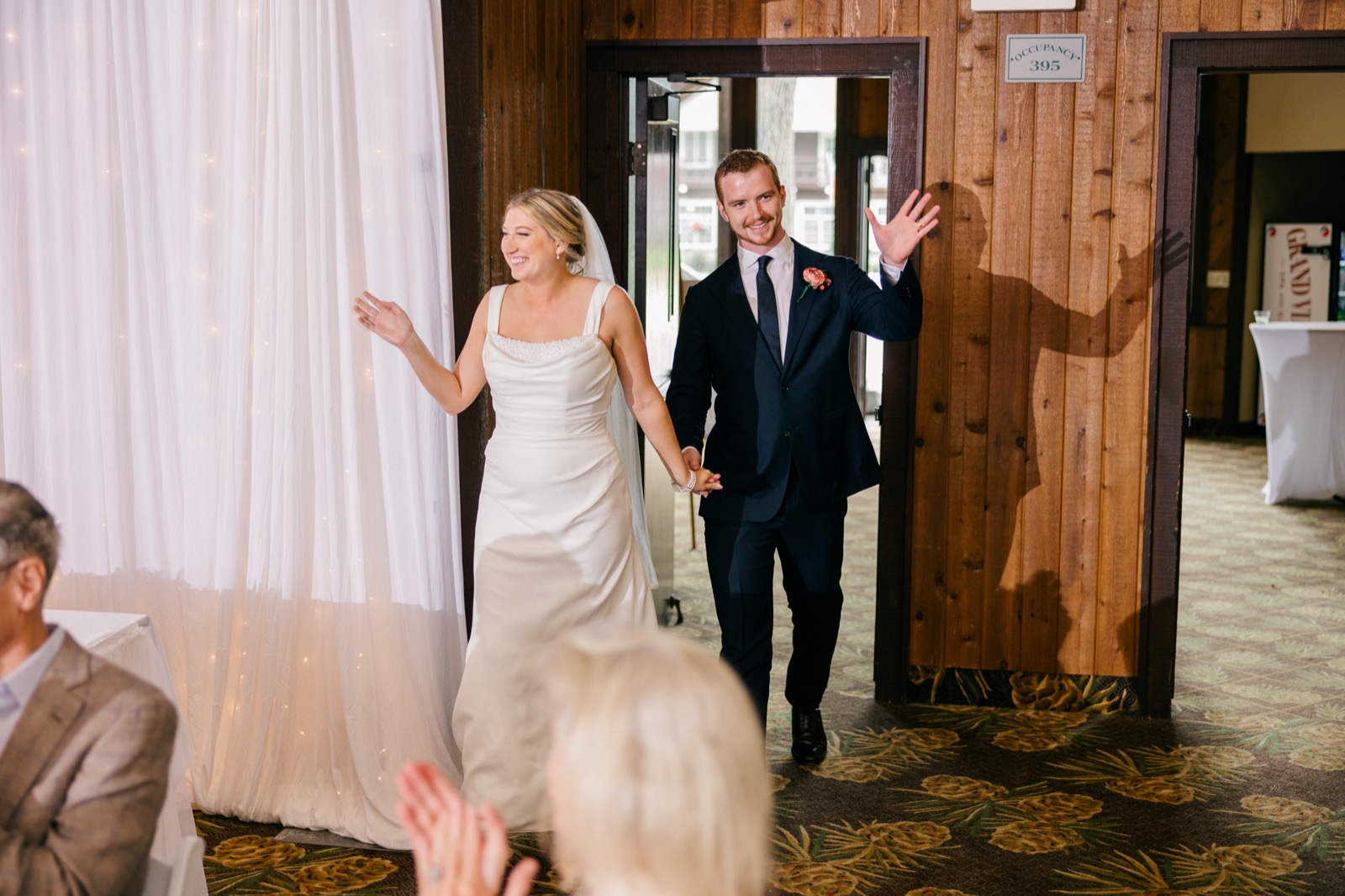 Monika and Mats raise their arms as they make their grand entrance into the reception, the groom's shadow cast on the wood-paneled wall behind them — Tim Larsen Photography, Brainerd Lakes MN