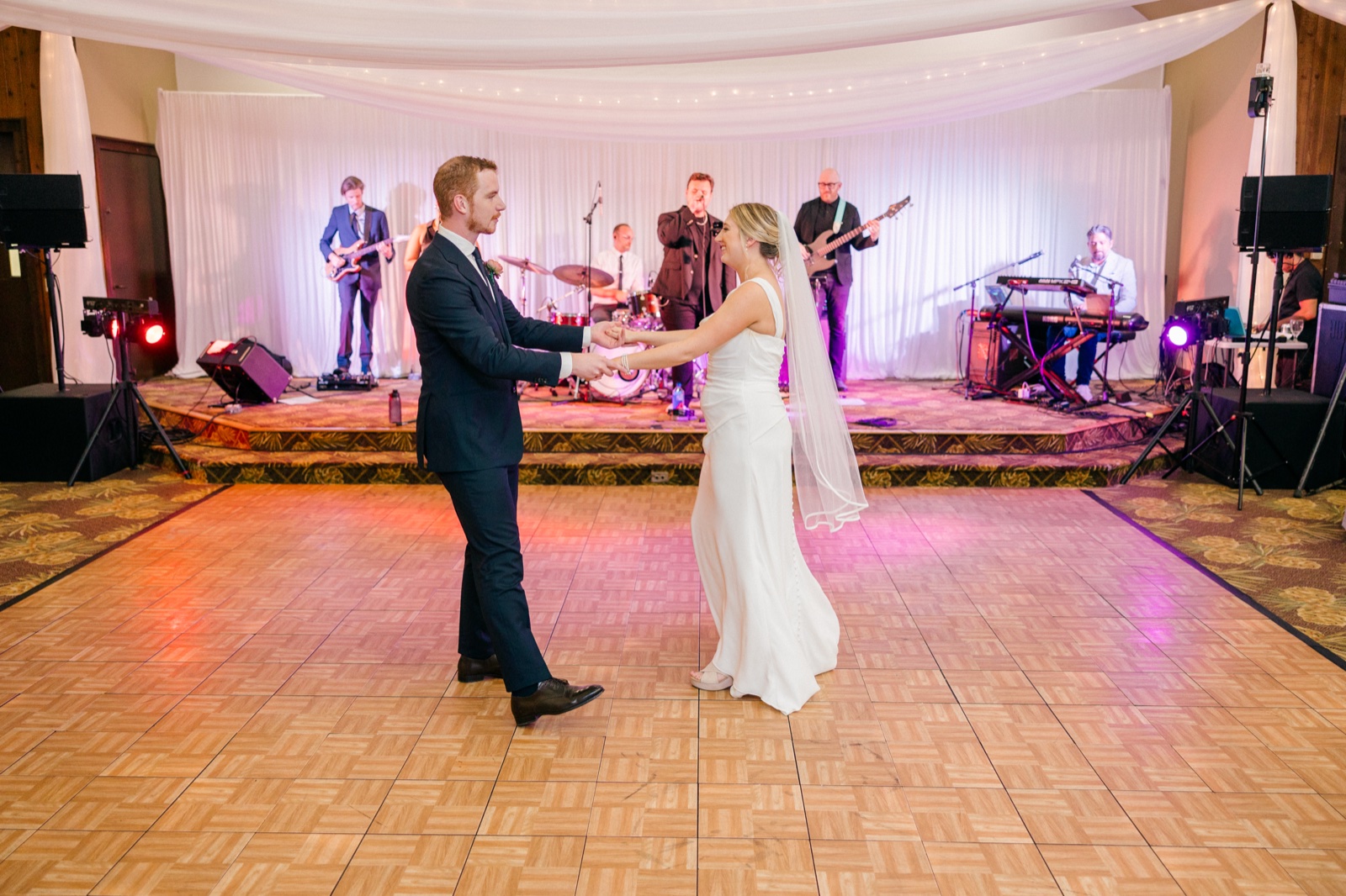 The bride and groom share their first dance on an empty parquet dance floor while a full live band plays on a draped stage behind them at Grand View Lodge — Tim Larsen Photography, Brainerd Lakes MN