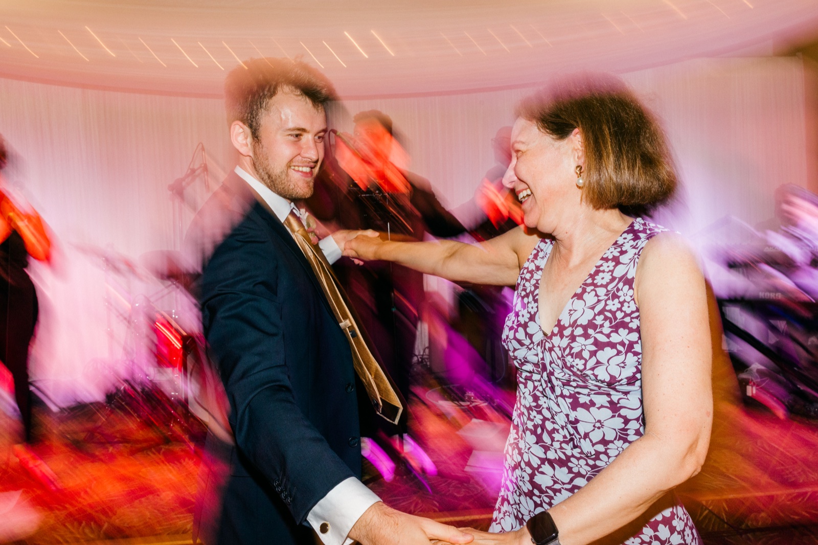 The groom and an older woman laugh together while dancing, surrounded by streaks of pink and magenta light from a dragged-shutter exposure — Tim Larsen Photography, Brainerd Lakes MN