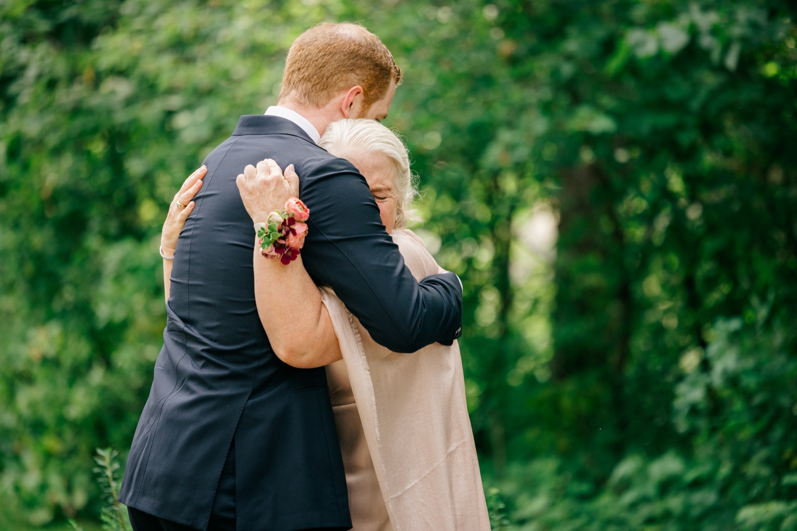 Mats embraces his mother on a garden path before the ceremony, her eyes closed against his shoulder, her corsaged hand resting on his back — Tim Larsen Photography, Brainerd Lakes MN