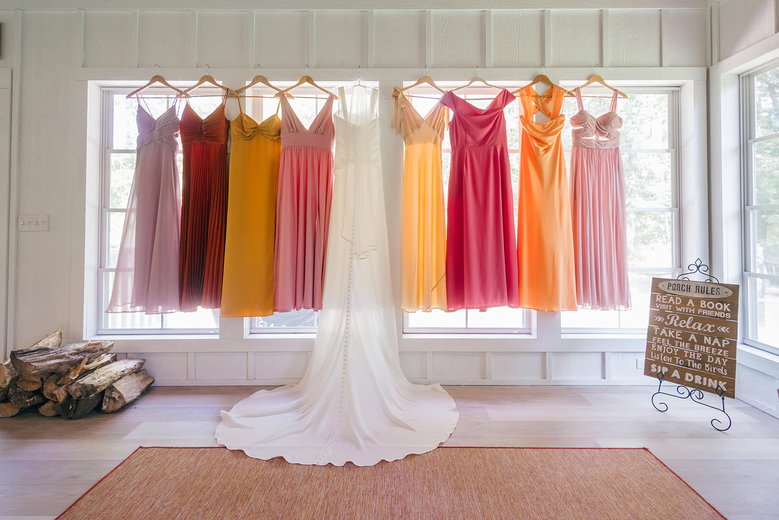 Bridesmaids dresses hanging in the window — rainbow of warm tones from burgundy to gold — Tim Larsen Photography, Brainerd Lakes MN