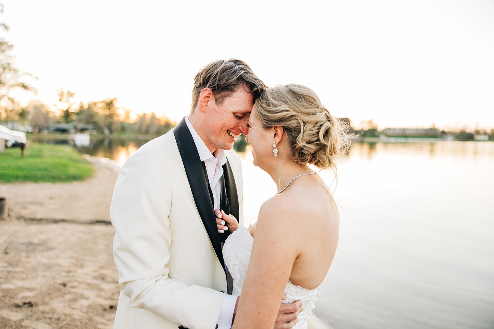 Forehead-to-forehead embrace on sandy shore with lake glowing warm behind — Cragun's Resort — Tim Larsen Photography, Brainerd Lakes MN