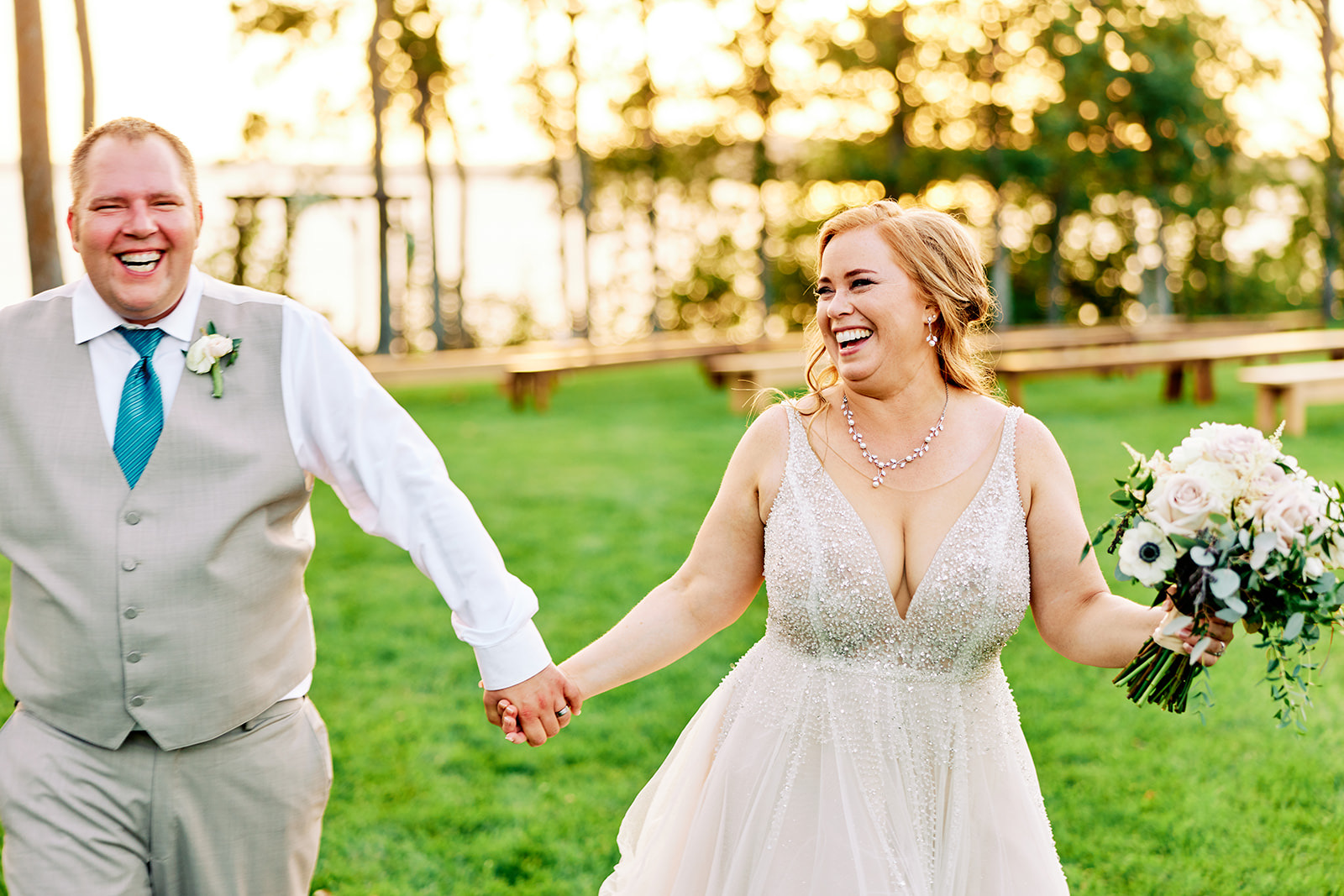Couple walking hand-in-hand toward camera with backlit trees and Gull Lake glowing behind — private cabin wedding — Tim Larsen Photography, Brainerd Lakes MN