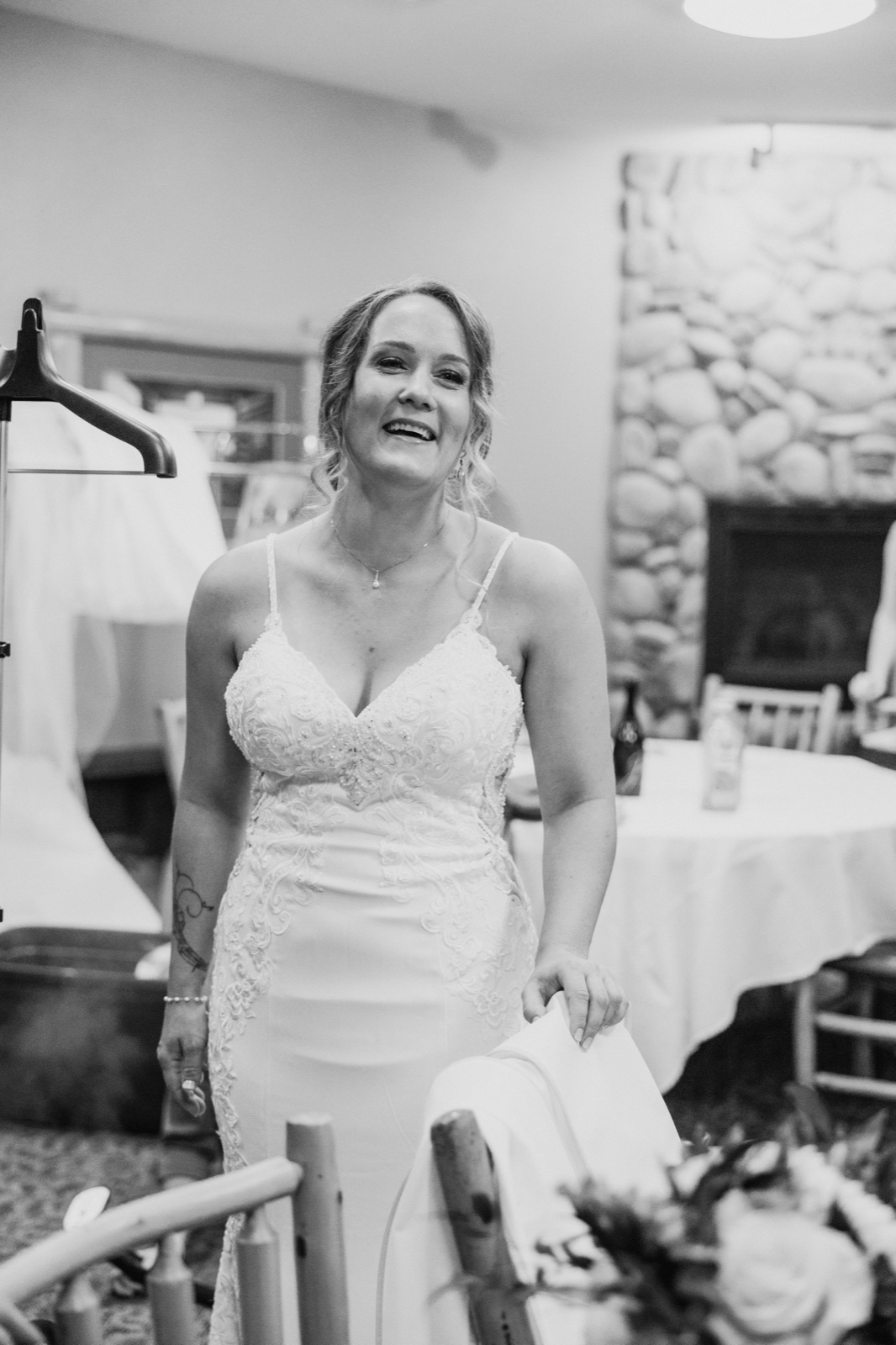 The bride laughs with her head tilted back, standing in her lace gown beside the stone fireplace of the Whitefish Lodge getting-ready room — Tim Larsen Photography, Brainerd Lakes MN