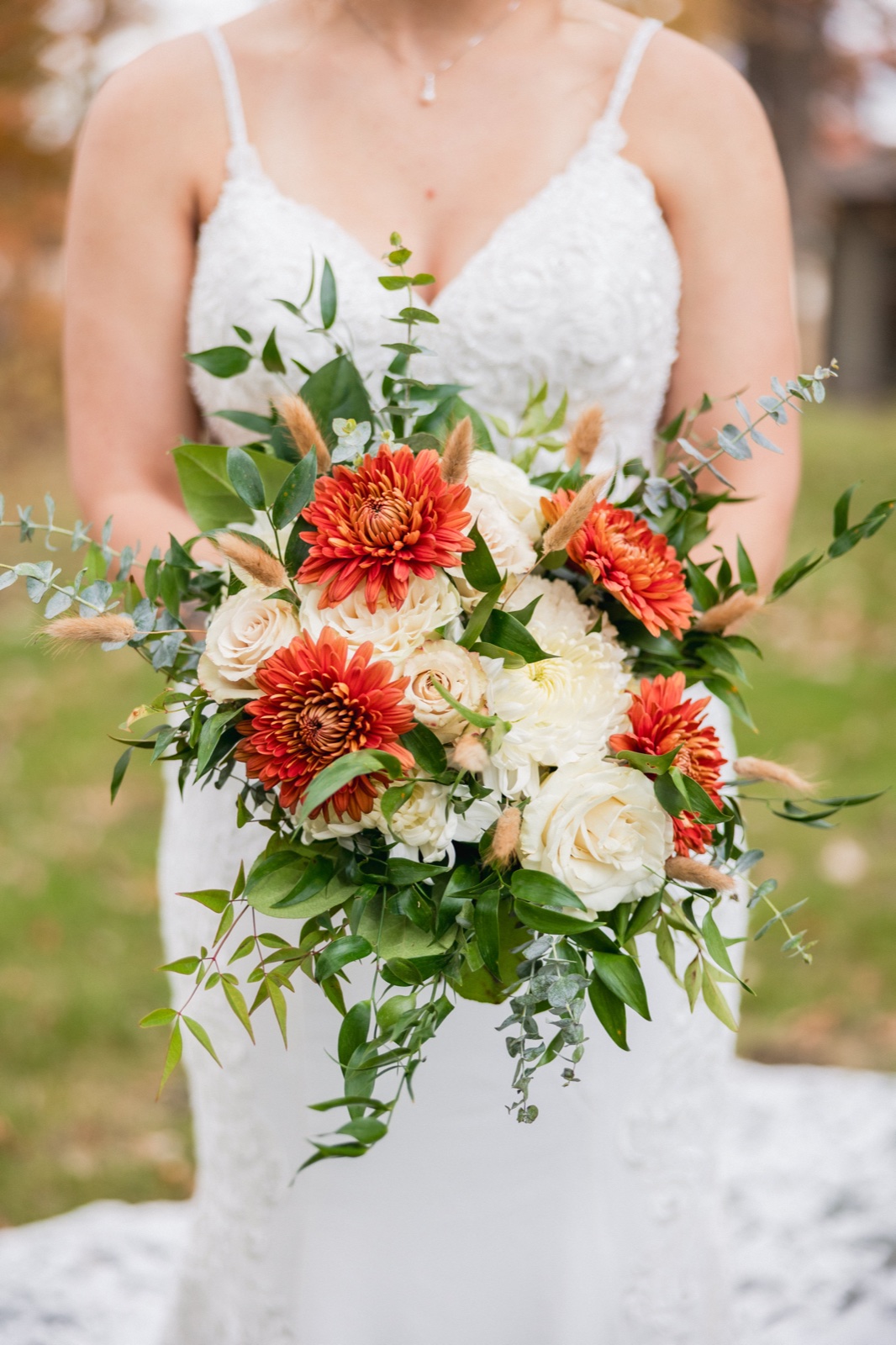 The bride holds a cascading autumn bouquet of orange chrysanthemums, ivory roses, eucalyptus, and bunny tails against her white wedding gown — Tim Larsen Photography, Brainerd Lakes MN