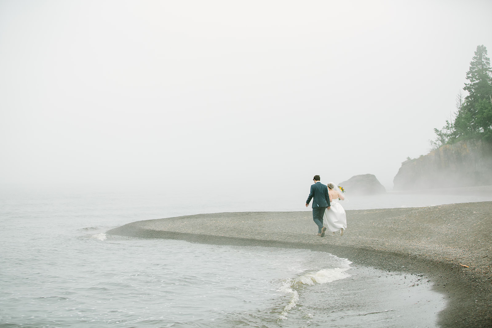 Couple running along the misty Lake Superior shoreline — North Shore wedding — Tim Larsen Photography, Brainerd Lakes MN