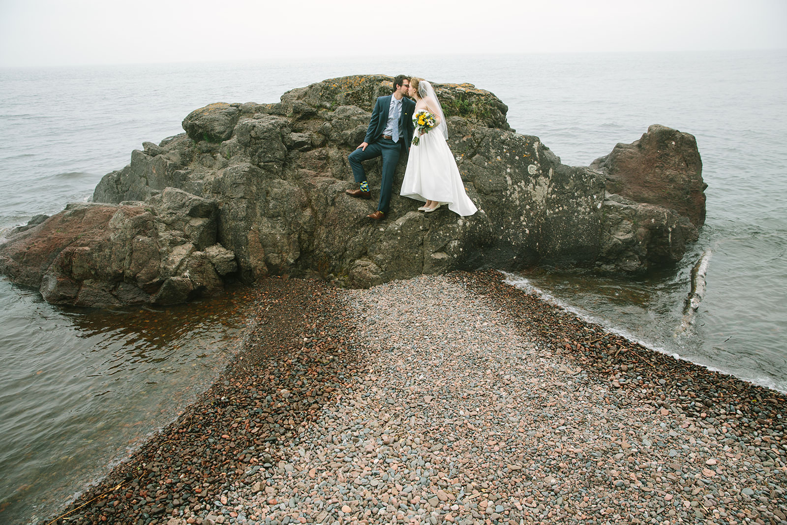 Couple kissing on a rock formation on the Lake Superior shore with wind-blown veil — Tim Larsen Photography, Brainerd Lakes MN