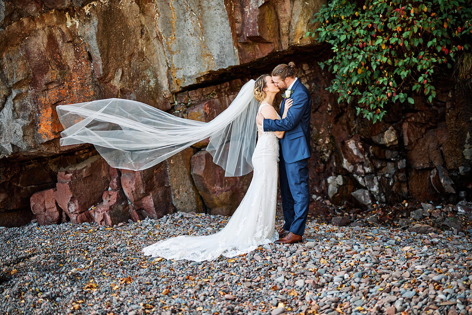 Couple kissing against red rock cliff on the North Shore — veil blowing in the wind — Tim Larsen Photography, Brainerd Lakes MN