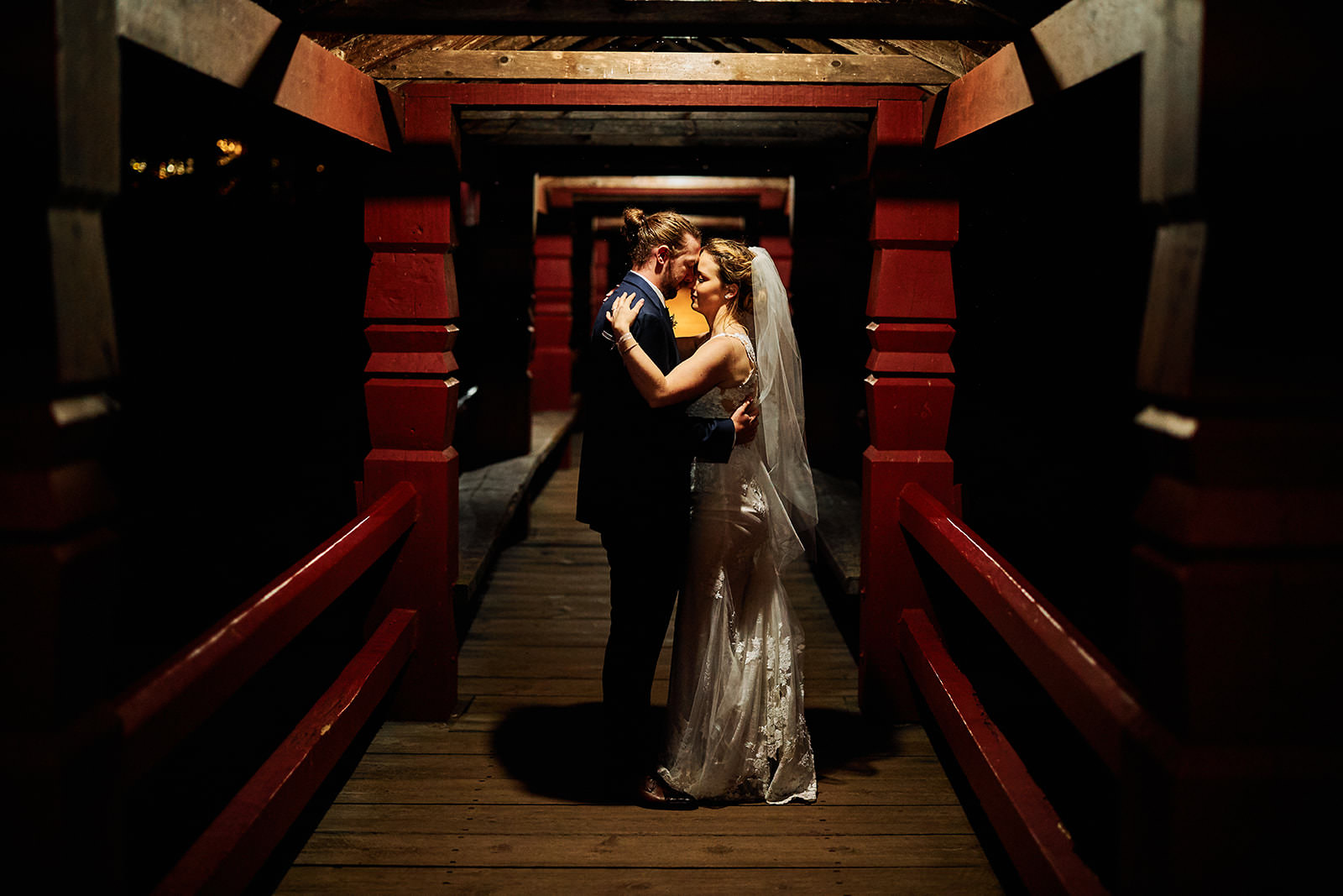 Couple kissing in a covered bridge at night — warm light on wooden walkway — Tim Larsen Photography, Brainerd Lakes MN