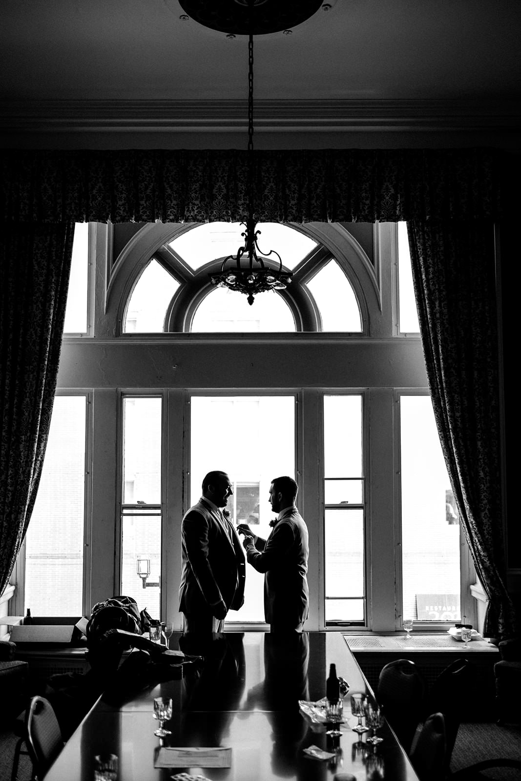 Two grooms sharing a quiet moment silhouetted against an arched window — Tim Larsen Photography, Brainerd Lakes MN